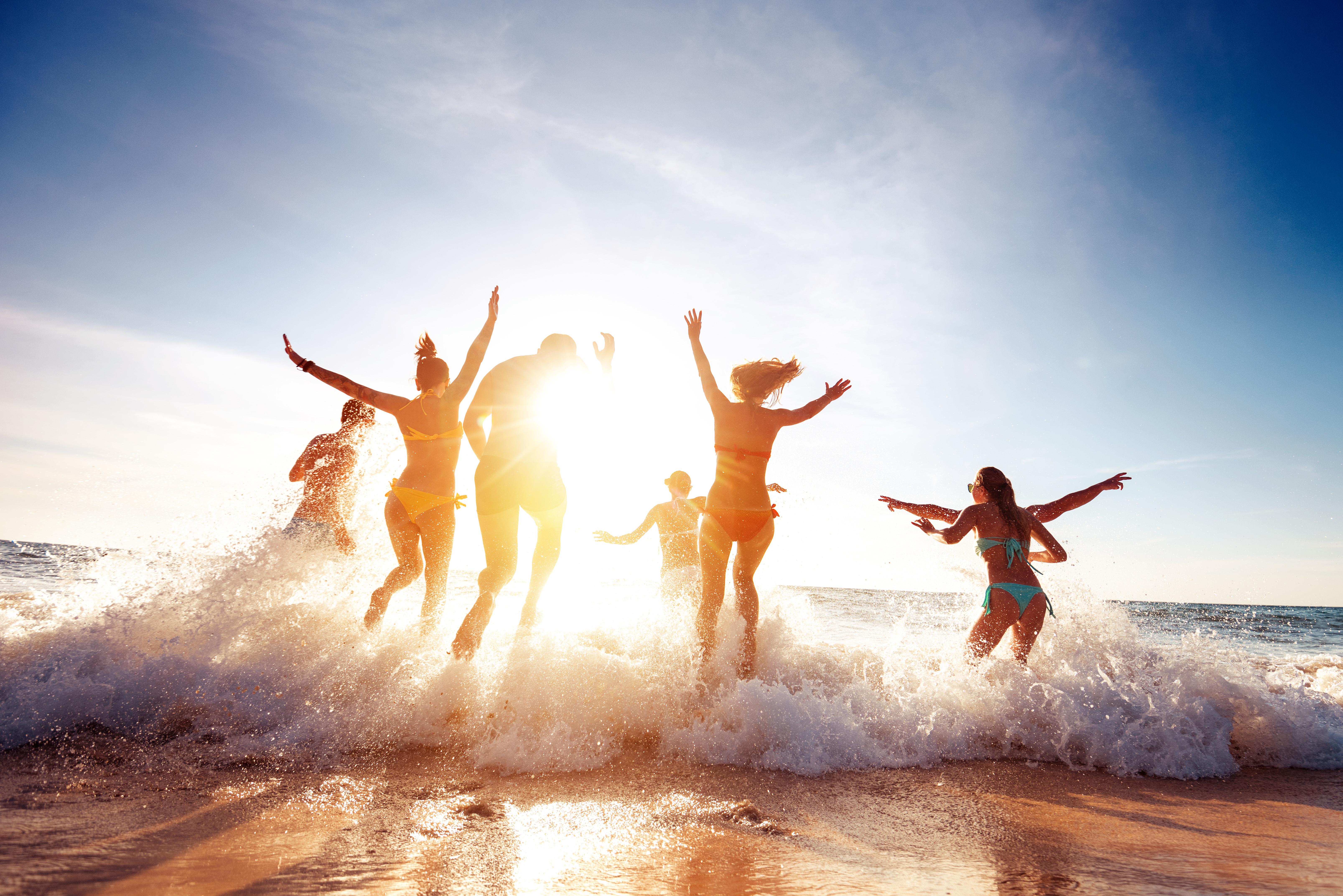 Big group of seven happy friends is having fun and runs at sunset beach to sun light and waves